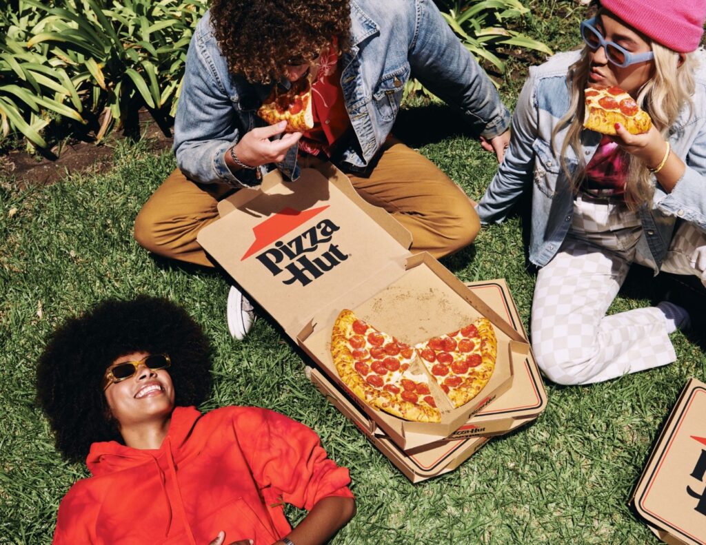 Three friends enjoying Pizza Hut pizza while sitting on the grass